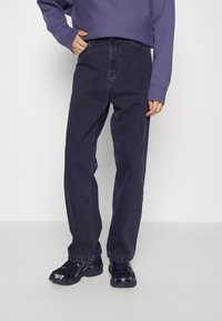 Mörkblå denimjeans med rak benform, ihopparade med svarta sneakers. Tyget har en mjuk textur och subtila sömnadsdetaljer.