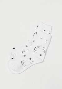 Calcetines blancos hasta el tobillo con un patrón de estrellas negras de diferentes tamaños. La textura parece suave, con un puño acanalado para mayor comodidad.