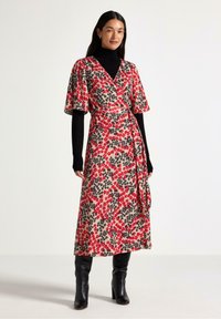 Abito a portafoglio floreale beige con motivi di fiori rossi e neri. Maniche a metà e vita con fiocco, abbinato a stivali neri al ginocchio.