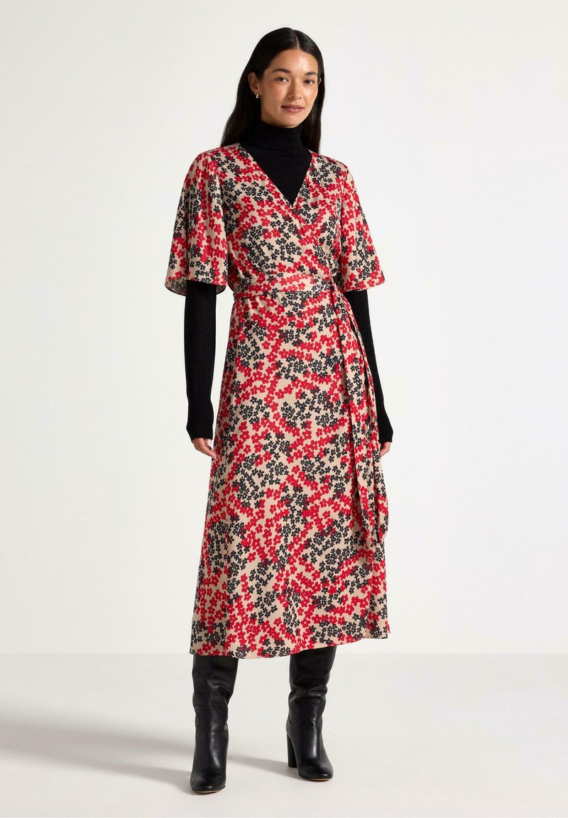 Abito a portafoglio floreale beige con motivi di fiori rossi e neri. Maniche a metà e vita con fiocco, abbinato a stivali neri al ginocchio.