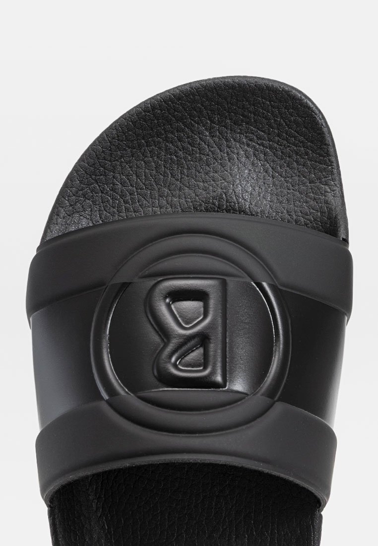 Schwarze Rutsch-Sandale mit einem strukturierten Riemen, der ein erhabenes Logo trägt. Das Fußbett ist glatt und die Sohle ist vollständig schwarz, was ein minimales Design bietet.