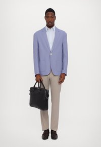 Light purple blazer with two front pockets, light blue shirt, beige trousers, holding a black leather briefcase, and brown loafers.