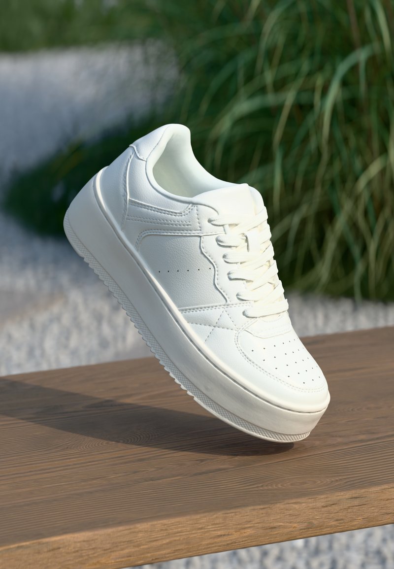 Vita lädersneakers med platt sula, rund tå och perforerade detaljer. Har snörning framtill och en minimalistisk design på en träytan.