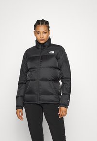 Black puffer jacket with high collar, quilted design, and zip closure. Features logo at chest and elastic cuffs for comfort.