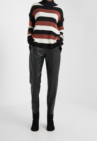 Pruhovaný pletený svetr v černé, bílé a rezavé barvě, doplněný o tailored černé kožené kalhoty a kotníkové boty. Měkká textura, uvolněný střih.