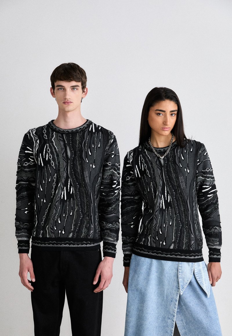 Zwart-wit gemusterde gebreide truien met lange mouwen, voorzien van textuurontwerpen. Model links in zwarte broeken, rechts in een denim rok.