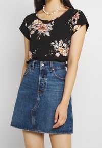 Top negro con estampado floral y mangas en forma de campana, combinado con una falda mini de mezclilla de cintura alta con dobladillo deshilachado y cierre de botón clásico.