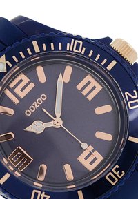 Montre bleu marine avec un boîtier rond, marqueurs d'heure et aiguilles en or rose. Comprend un guichet de date à 6 heures et une lunette texturée.