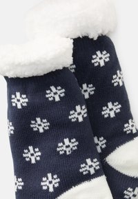 Chaussettes navy avec un revers blanc duveteux et un motif de flocon de neige blanc. Fabriquées en matériau doux, elles offrent un ajustement confortable et une texture côtelée.