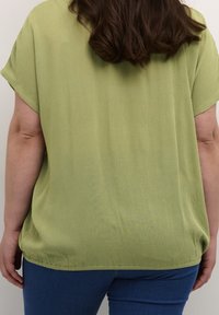 Løst siddende top i lys grøn, struktureret stof med korte ærmer. Kombineret med blå jeans, som viser en afslappet silhuet.