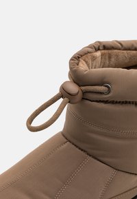 Botte imperméable marron avec un col doux et rembourré, cordon de serrage ajustable. Présente des coutures renforcées et une finition en tissu texturé.