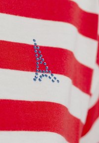 Striped t-shirt in red and white featuring a blue rhinestone embellishment shaped like the letter "A" on the front. Soft cotton texture.