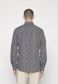 Maglietta a righe bianche e nere con motivi di testo verticali, maniche lunghe e colletto. Realizzata in tessuto, presenta un orlo dritto nella parte inferiore.