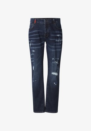 Jeans in denim blu scuro con taglio dritto, caratterizzati da toppe consumate, schizzi di vernice e una piccola etichetta rossa sulla cintura.