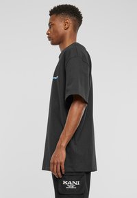 Sort bomulds t-shirt med løs pasform, kortærmede, og blå grafik på brystet. Bæret med matchende cargo shorts med hvid tekst.