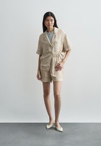 Sada krátkeho rukáva a šortiek s béžovým vzorom a sťahovacou šnúrou v páse. Modelka má pod tým sivý top a krémové nazúvacie topánky.