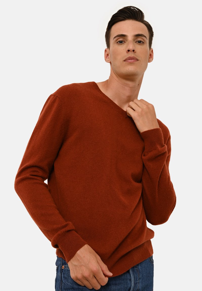 Maglione a V colore ruggine realizzato in un morbido tessuto a maglia, con maniche lunghe e polsini a coste, abbinato a jeans in denim blu.