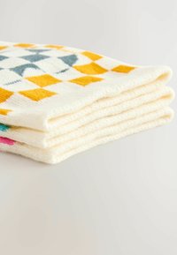 Staplade, färgglada handdukar med gula, blå och rosa geometriska mönster på en krämfärgad bakgrund, vilande på en ljus yta.