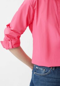 Korte mouwen roze shirt van lichtgewicht stof, met knoopmanchetten en een ontspannen pasvorm. Draagt met blauwe denim jeans.