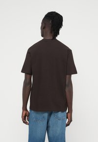 Καφέ κοντομάνικο βαμβακερό T-shirt με άνετη γραμμή, κλασικό στρογγυλό λαιμόκοψη και χωρίς ορατά σχέδια ή μεταλλικά στοιχεία.