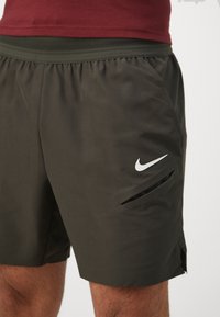 Nike urheilushortsit tummanvihreänä, valmistettu kevyestä kankaasta. Sisältää sivutaskut ja valkoisen Nike-logon edessä. Elastinen vyötärö.