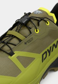 Ελαιοπράσινα αθλητικά παπούτσια με μαύρους κορδόνες, με υφή στην επιφάνεια, κίτρινες λεπτομέρειες και ετικέτα GORE-TEX για αντοχή στις καιρικές συνθήκες.