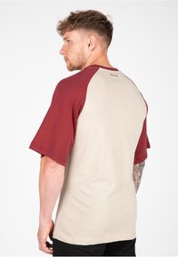 Korte mouwen, bicolor t-shirt met een beige lichaam en bordeauxrode raglanmouwen. Zachte katoenstof met een ronde halslijn en gestikte details.