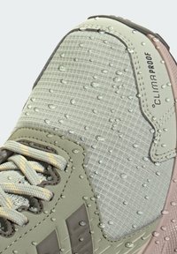 Lichtgrijze waterbestendige sneaker met gestructureerde stof, rubberen accenten en zichtbare waterdruppels. Voorzien van veters en logodetail.