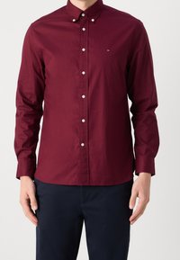 Burgundowa koszula z długim rękawem, zapinana na guziki, z klasycznym kołnierzykiem, białymi guzikami oraz małym haftowanym logo na piersi. Wykonana z bawełny.
