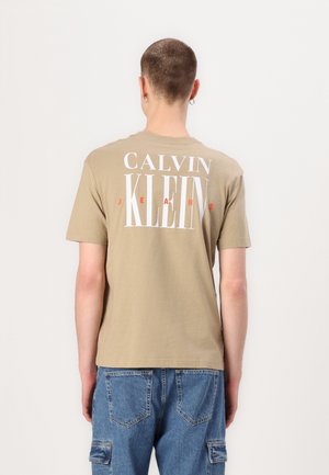 Beżowa bawełniana koszulka z krótkim rękawem, z okrągłym dekoltem, z dużym białym i czerwonym napisem na plecach "CALVIN KLEIN JEANS".