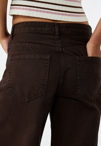 Brune denim jeans med høj talje, der har en glat tekstur og to baglommer. Stilen inkluderer lige ben og diskret syning.
