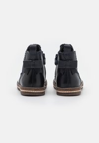 Bottines en cuir noir avec une surface lisse, des bords festonnés et des accents de nœud à l'arrière. Présentent une semelle cousue et un petit talon.