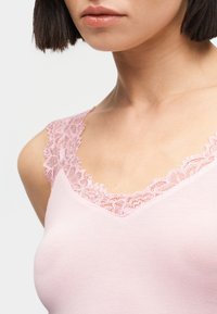 Γυναίκα που φοράει ροζ τοπ χωρίς μανίκια με δαντέλα κατά μήκος της λαιμόκοψης και των τιράντων στους ώμους.