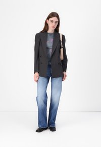 Blazer noir à rayures, design double toilé, porté sur un top floral transparent. Un jean évasé bleu clair et des ballerines noires complètent la tenue.