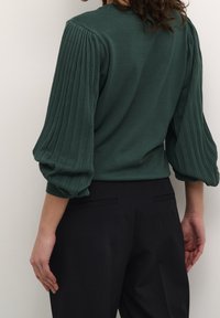 Haut tricoté vert avec des manches bouffantes côtelées, complété par un design de corps lisse. Associé à un pantalon noir ajusté pour un look élégant.