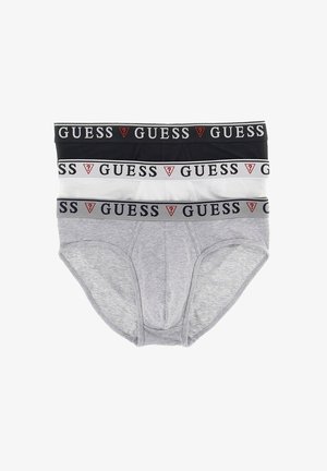 Caleçons blancs en coton avec une ceinture élastique noire portant le logo "GUESS", présentant une coupe classique et une texture lisse. Le modèle pose sur un fond neutre.