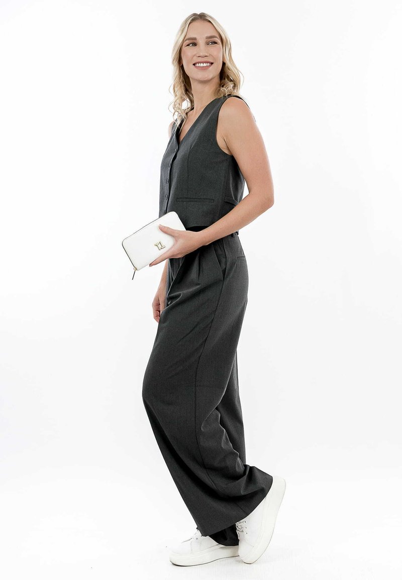 Gray sleeveless jumpsuit with vertical seams, two front pockets, and a relaxed fit. Paired with a white wallet and white sneakers.