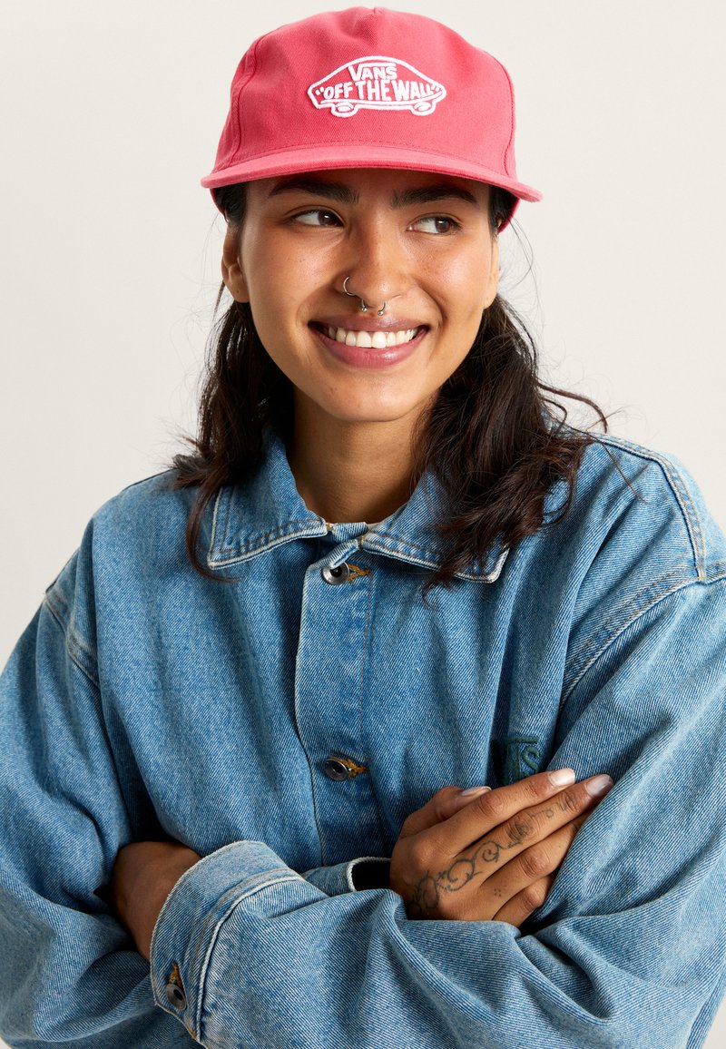 Gorra roja con el logo blanco "VANS OFF THE WALL", combinada con una chaqueta de mezclilla azul. La chaqueta tiene un corte relajado y botones resistentes.