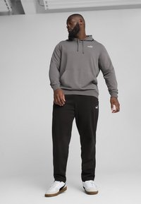 Grå hættetrøje med frontlomme og snor,parret med sorte sweatpants. Hvide sportsko med en brun sål og sorte accenter.