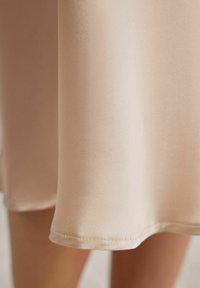 Robe en satin rose clair avec une texture lisse, comportant un ourlet simple. Le tissu semble doux et légèrement brillant.