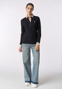 Polo nero a maniche lunghe con colletto beige, due bottoni e logo ricamato. Abbinato a jeans a gamba larga blu chiaro e sneakers bianche.