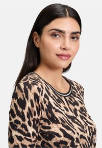 Top a maniche lunghe con motivo leopardato, caratterizzato da un collo rotondo con profilo nero, tessuto morbido e design aderente.