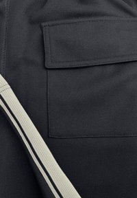 Zwart stoffen met een gestructureerde afwerking, een opgestikte zak en een zijnaad met een wit- en zwartgestreept detail.
