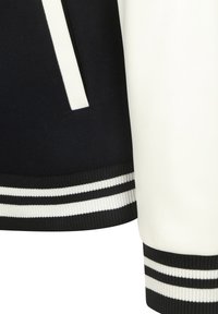 Zwart-wit sportjack met contrasterende mouwen, voorzien van ribgebreide manchetten met dubbele witte strepen en een strak, modern ontwerp.