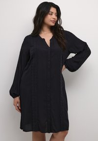 Vestido negro de botones, hecho de una tela ligera, con mangas largas, escote en V y un intrincado detalle de encaje a lo largo de los costados.