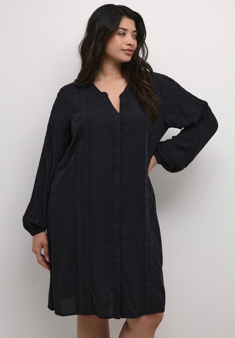 Vestido negro de botones, hecho de una tela ligera, con mangas largas, escote en V y un intrincado detalle de encaje a lo largo de los costados.
