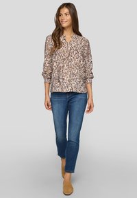 Leichte Langarmbluse mit braun-beigem Animal-Print, rundem Ausschnitt und elastischen Bündchen, kombiniert mit blauen Jeans und beigen Loafers.