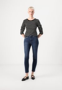 Black and white striped top with long sleeves, paired with dark blue skinny jeans and black flat shoes with decorative accents.