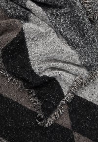 Couverture en mélange de laine arborant un motif géométrique aux tons noirs, gris et marron, avec des bords effilochés pour la texture.