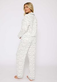 Ensemble de pyjama blanc avec un motif d'étoiles en bleu et vert. Comprend un haut à manches longues avec boutons et un pantalon assorti avec une finition décorative.